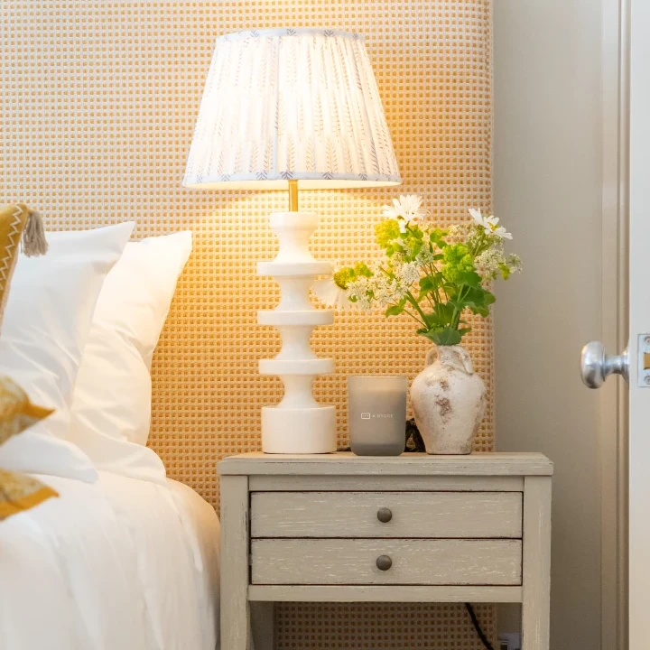 A vibrant yellow fabric headboard is the perfect backdrop to a sculptural table lamp and posy of flowers.
